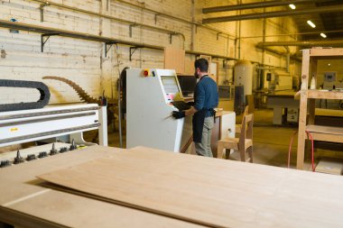 CNC router makinesiyle çalışan bir adamın arka görüntüsü. Bir sürü endüstriyel makine ve marangozluk projeleri için aletleri olan büyük ve geniş bir marangoz dükkanı.