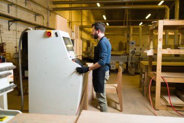 Büyük bir marangozhanede odun kesmek için CNC yönlendirici kullanan İspanyol bir işçinin yan görüntüsü. Erkek marangoz marangozluk yapıyor.