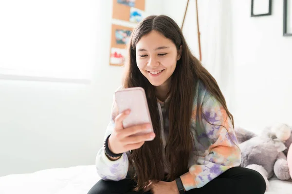 坐在卧室里和朋友用智能手机发短信的少女笑着 在社交媒体平台上聊天的漂亮少女 — 图库照片
