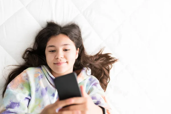 漂亮的少女躺在床上为社交媒体自拍 可爱而快乐的少女用智能手机给朋友发短信 — 图库照片