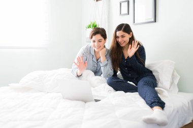 Oldukça iyi arkadaşlar merhaba diyor ve bilgisayardaki bir video görüşmesi sırasında arkadaşlarıyla konuşuyor. İki kadın, aileleriyle yatakta görüntülü konuşma yapıyor. 