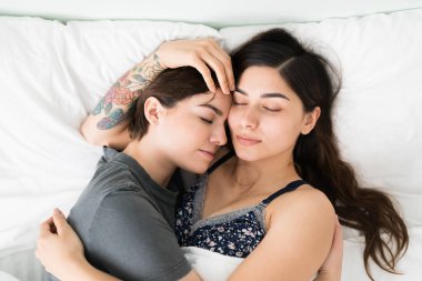 Çekici lezbiyen çift yatak odalarında uyurken birbirlerine sarılıyorlar. Romantik genç kız arkadaşlar yatakta uzanırken sakin görünüyorlar. 