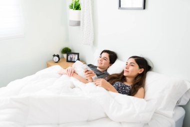 Genç eşcinsel kadın yatakta romantik bir film izlemek için akıllı televizyon kumandasını kullanıyor. Gülümseyen lezbiyen çift yatak odasında dizi seyrediyor. 