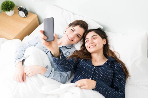 20多岁的拉丁女人在睡前和她的高加索好友睡在一起 然后用智能手机自拍 — 图库照片