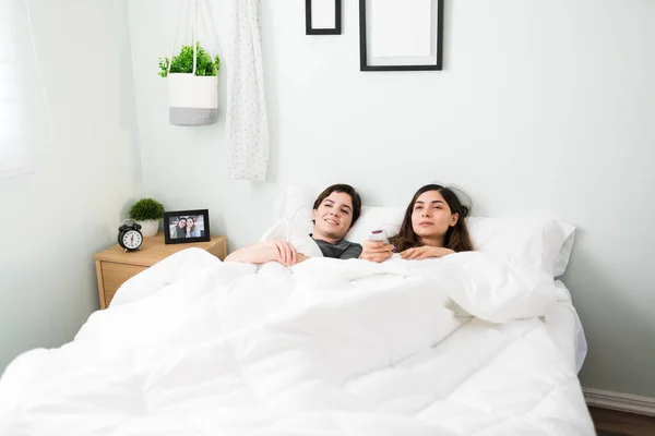 一对年轻的女同性恋夫妇躺在床上看电影 两个同性恋女人躺在卧室里 在聪明的电视上寻找网上观看的东西 — 图库照片
