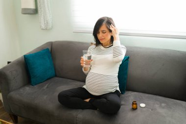 Acı çeken hamile bir anne güçlü bir migren ağrısı çekiyor ve başını ovuyor. Çekici hamile kadın baş ağrısı çekiyor ve ağrı kesici almak üzere.