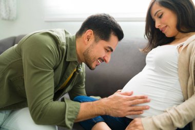 Heyecanlı müstakbel ebeveynler koltukta dinleniyor. Çekici bir adam kanepede dinlenirken hamile karısının karnına dokunuyor ve onunla konuşuyor.