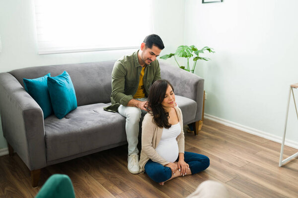 Красивая жена расслабляется и наслаждается массажем плеч. Красивый мужчина массирует спину красивой беременной женщине, сидя на диване