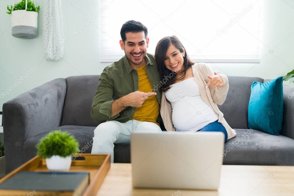 Happy and excited husband and pregnant wife revealing to their family and friends about their new baby in a video call. Woman showing their round belly during an online video chat