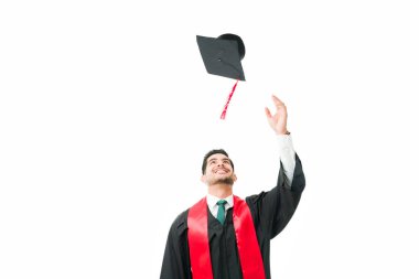 Heyecanlı genç erkek mezun mezuniyet şapkasını havaya fırlatıyor ve üniversite diplomasını aldıktan sonra kutlama yapıyor.