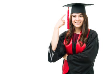 Mezuniyet elbisesi giymiş, şapkasını ve kırmızı püskülünü gösteren zeki bir genç kadın. Üniversite ya da yüksek lisans derecesi almak üzere olan güzel kız.