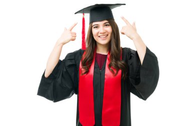 20 'li yaşlarda mutlu bir kadının portresi. Elbise giyiyor ve mezuniyet şapkasını gururla gösteriyor. Mezuniyet törenine katılan genç bir kız.