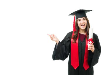 Beyaz arka planda siyah bir elbise, kep ve kırmızı püsküllü genç bir bayan mezuniyet portresi. Güzel bir kadın gülümsüyor ve boşluğu işaret ediyor.