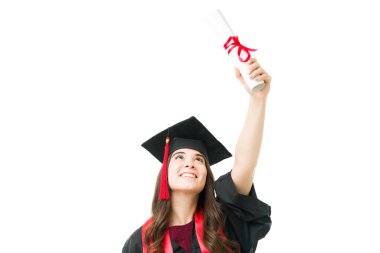 Mezuniyet töreninde siyah bir elbise ve kep giyerken gülümseyen ve havada yükselen güzel bir üniversite mezunu.