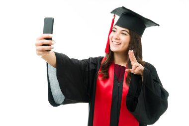 Güzel ve mutlu genç bir kadın mezuniyet gününü kutlamak için sosyal medyada akıllı telefonuyla fotoğraf çekiyor.