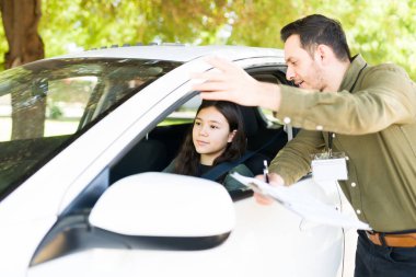 Latin bir erkek eğitmenin beyaz bir kızla konuşmasının ve sürüş dersleri için ona bazı talimatlar vermesinin yan görüntüsü