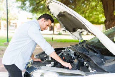 30 'lu yaşlardaki yakışıklı İspanyol bir adam bozuk bir arabanın motorunu kontrol ediyor. Erkek sürücünün araba sorunu var 