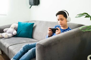 İlkokul öğrencisi, okul tatilinde kulaklık takıyor ve akıllı telefondan internet videoları izliyor.