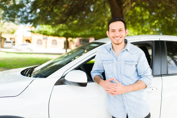 Portrait of a good-looking man in his 30s looking happy and standing next to his car. Latin guy ready to start working as a taxi driver