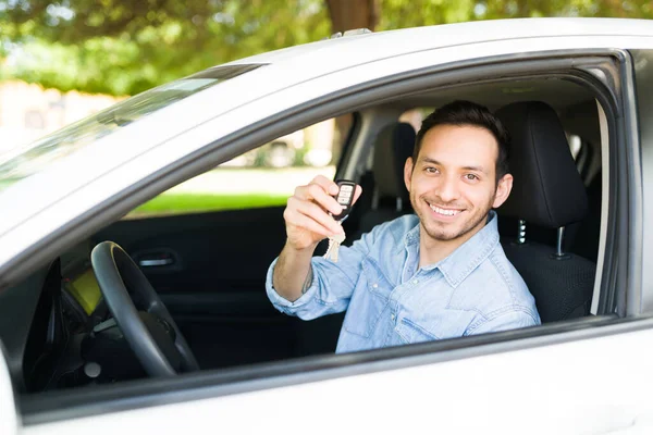 Good-looking latin man sitting in the driver\'s seat and showing his new car keys. Male taxi driver happy to start working on a mobile transportation app