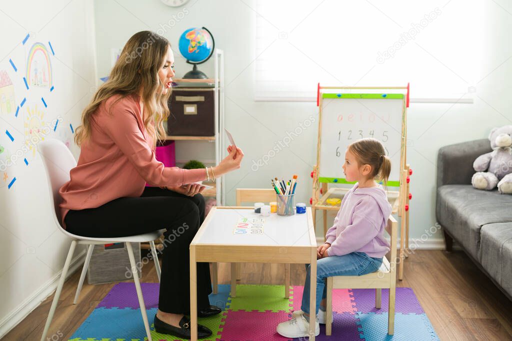 Smart mom teaching the alphabet to a beautiful elementary girl sitting at the kid's table. Mother and little daughter at a homeschool program