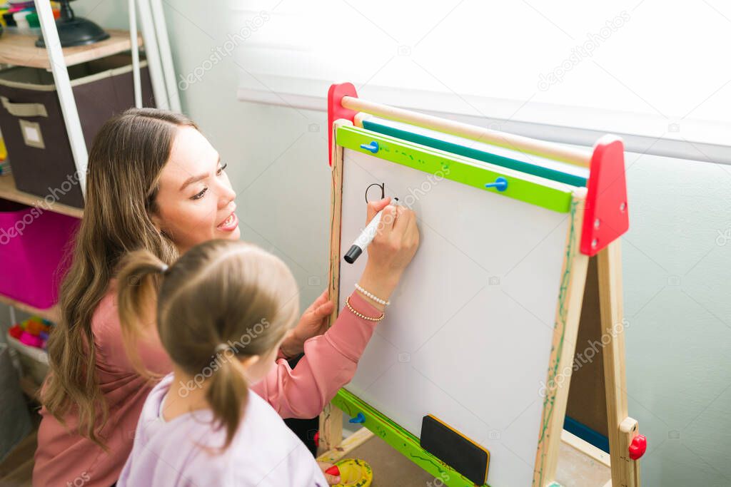 Female tutor writing the alphabet on a small blackboard during a tutoring class with a caucasian girl. Parent homeschooling her preschool daughter