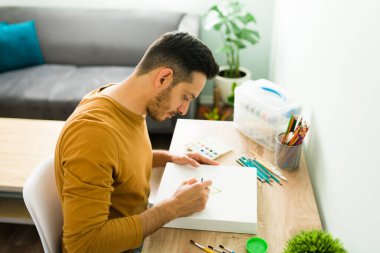 Evde boş bir gün geçirirken mutlu bir adamın portresi. İyi bir ruh sağlığı çalışanını, erkeği, erkeği, bir kişiyi korumak için suluboya resim yapan pozitif Latin bir adam., 