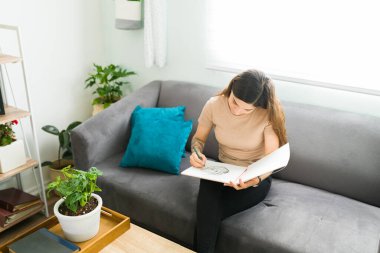 Evde dinlendirici bir günde elinde kalemle çizim yapan 20 'li yaşlarda İspanyol bir kadın. Kanepede otururken hobisine çalışan genç bir kadın.