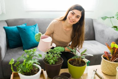 Happy young woman smiling while holding a watering can to water her houseplants. Good-looking woman enjoying her leisure time at home