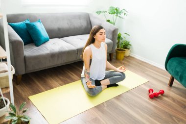 Relaxed young woman starting her breathing exercises while doing an easy yoga pose. Attractive woman meditating at home for a relaxing day