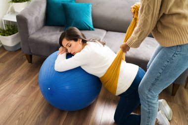 Güzel, hamile bir anne, gözleri kapalı ve rahatlarken bir spor topu ve hamile karnını kaldırmak için ebesiyle bir rebozo kullanıyor.