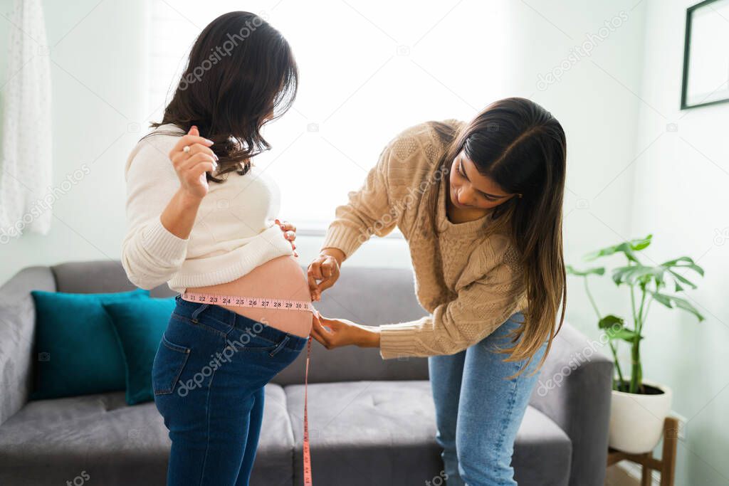 Sie view of a beautiful latin midwife or doula measuring with a tape the round naked belly of a pregnant caucasian woman 