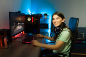 Gyönyörű fiatal nő fülhallgatóval mosolyog és ül előtt egy játék PC neon led fények a hálószobában