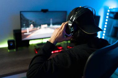 Kulaklıklı bir erkek oyuncunun oyun bilgisayarında oyun oynamaya hazırlandığı arka görünümü.