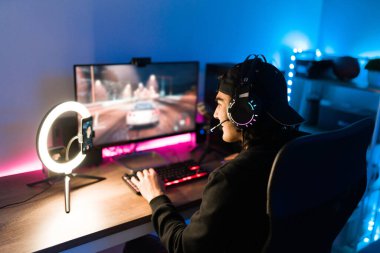 Latin genç adam canlı yayında akıllı telefondan gülüyor. Yakışıklı oyuncu bilgisayarında neon ışıklı bir video oyunu oynarken kendini mutlu hissediyor.