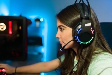 Kulaklıklı ve mikrofonlu güzel genç bir kadın online video oyunu oynamaya odaklanıyor. Lider ışıkları olan bir oyun bilgisayarı kullanan bayan oyuncu