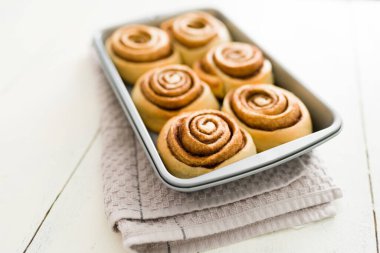 Taze tarçınlı rulo. Lezzetli ve mükemmel tarçınlı rulo beyaz ahşap mutfak masasının üzerindeki bir fırın tepsisinde soğuyor.
