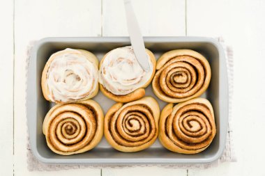 Bıçakla dekore edilmiş lezzetli tarçınlı rulo. Ahşap mutfak masasındaki metal bir fırın tepsisinde tarçınlı ve şekerli çörek.