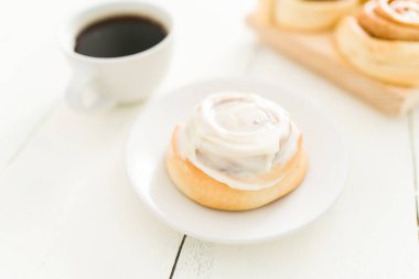Tatlı tabağında lezzetli bir tarçınlı rulo ekmeği sıcak bir fincan kahvenin yanına koy. Tatlı rulo şeker kahvaltıda yemeye hazır.
