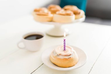 Doğum günü dileği tut. Beyaz kremalı tarçınlı börek ve küçük bir doğum günü mumu. Mutfak masasındaki pasta standında kahve fincanının yanında nefis börekler.