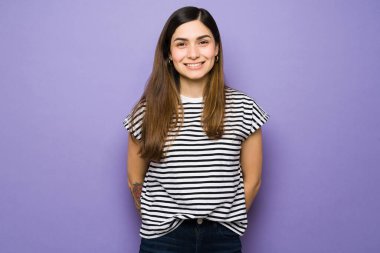 Işıl ışıl gülümseyen, mor bir arka plan karşısında duran İspanyol genç kadın. 20 'li yaşlarındaki çekici bir kadın günlük kıyafetler giyiyor ve mutlu görünüyor.