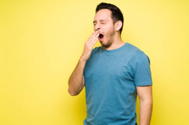 Uykulu İspanyol adam esniyor ve uyumayı bekliyor. Parlak bir arkaplan önünde yorgun düşmüş Latin bir adam