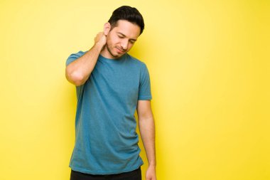 Boynu ve omuzları ağrıyan yakışıklı bir adam. Stresli Latin bir adam başının arkasını ovuyor ve boynundaki yaralanmadan şikayet ediyor.