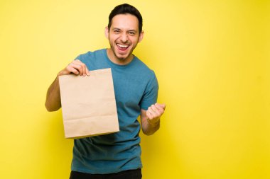 Heyecanlı İspanyol adam öğle yemeği için yemeğini aldığı için mutlu. Latin adam gülümsüyor ve elinde yiyecek dolu kahverengi bir çanta tutuyor.