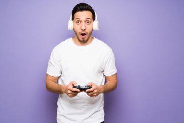 Şaşırmış ve heyecanlı kulaklıklı adam heyecan içinde bağırıyor ve uzaktan kumandayla çevrimiçi bir video oyunundan zevk alıyor.