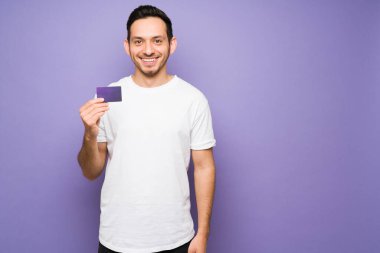 Heyecanlı yakışıklı adam ilk kredi kartını aldığı için mutlu. Elinde mor bir kredi kartı olan beyaz tişörtlü, gülümseyen genç adam. 