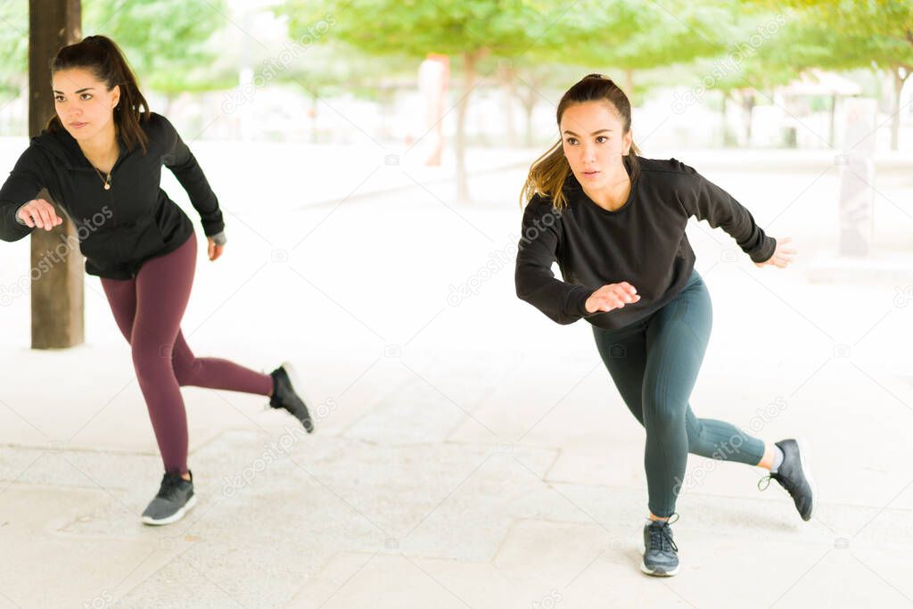 Beautiful hispanic woman in their 30s doing lateral bounds during a HIIT session outdoors. Sporty women in activewear exercising with a cardio workout