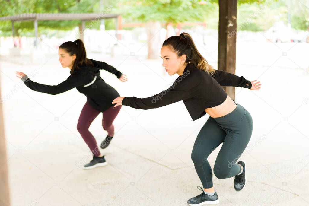 Attractive women doing lateral bounds during a cardio workout at the park. Fit latin women exercising with a HIIT routine outdoors