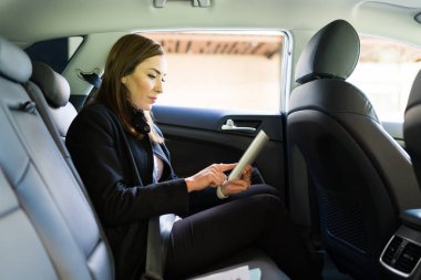 Çekici iş kadını tablet kullanıyor ve taksinin arkasında otururken çalışıyor. İş kadını şehirdeki ofisine doğru yola çıktı.