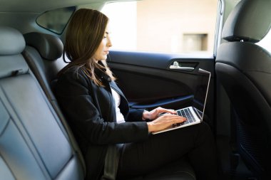 Profesyonel iş kadını laptopunu kullanıyor ve işe gidip gelirken çalışıyor. İş kadını, ofise giderken bir taksinin arkasında yolcu olarak seyahat ediyor.